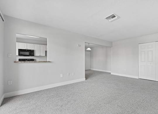 A spacious living room with a grey carpet and white walls.
