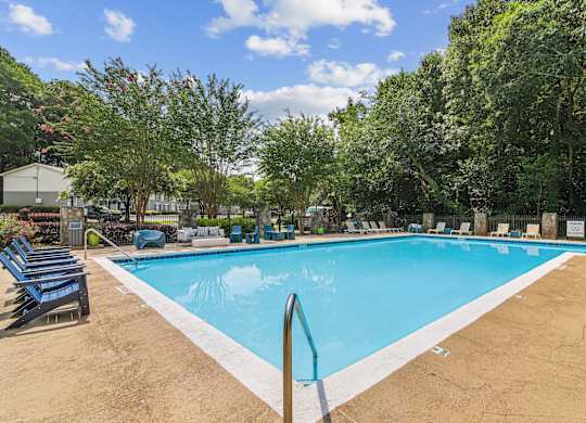 A large outdoor swimming pool surrounded by trees and lounge chairs.