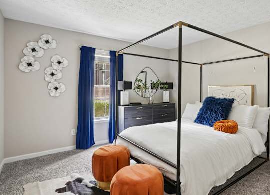 A bedroom with a four poster bed and a window with blue curtains.