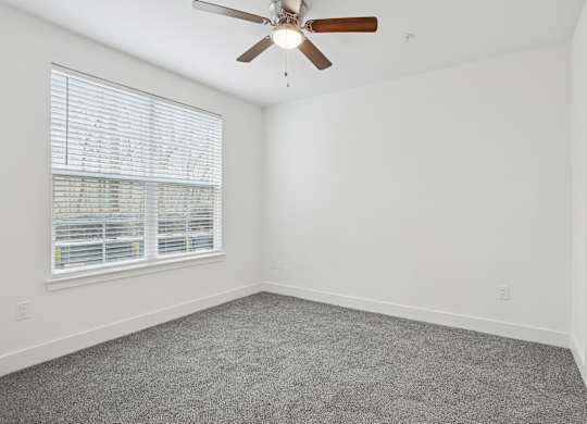 A room with a ceiling fan and a window with blinds.