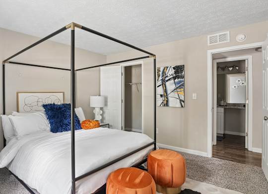 A bedroom with a four poster bed and a small orange ottoman.