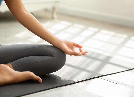 A person is sitting cross-legged on a yoga mat with their hands in a prayer position.