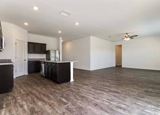 A spacious room with a kitchen area and a ceiling fan.