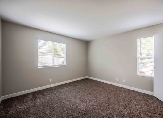 an empty room with carpet and two windows
