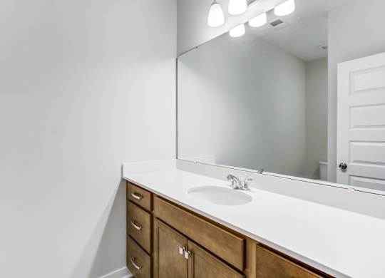 Charleston, SC, Apartments - Sumner Village - Bathroom with Granite Vanity Countertop, Large Mirror, Bright Lights, and Wooden Cabinetry.