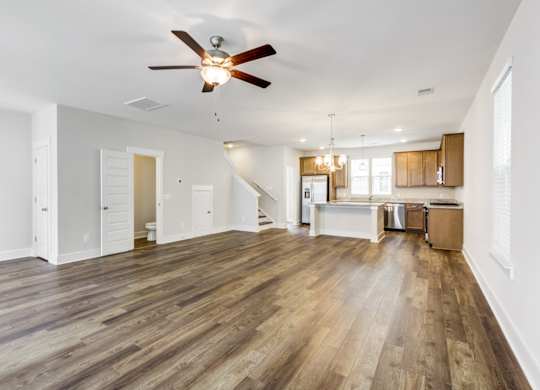 Single Family Homes in North Charleston, SC - Sumner Village - Open-Layout Living Room with Vinyl Plank Flooring, Ceiling Fan, Toilet, Staircase, and View of Kitchen Area.