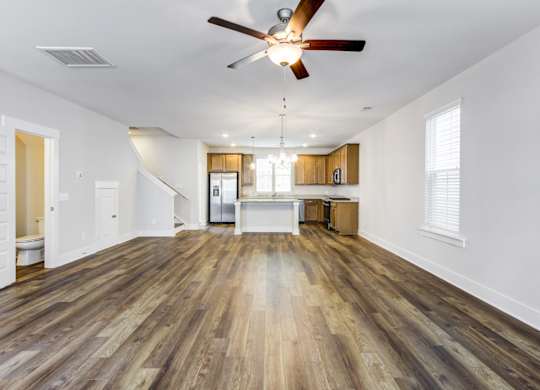 Park Circle Home Rentals - Sumner Village - Open-Floor Living Room With Vinyl Plank Flooring, Ceiling Fan, And Easy Access To A Toilet And Kitchen