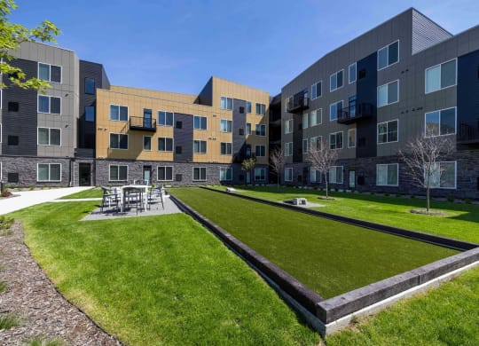 a grassy area with tables and chairs in front of an apartment building