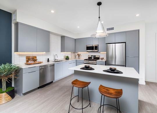 A modern kitchen with a bar stool and a hanging light fixture.