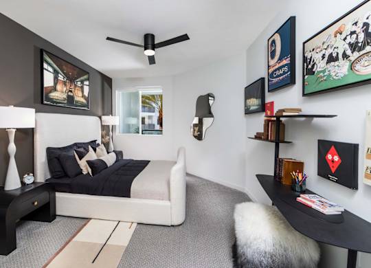 A bedroom with a bed, a table, and a ceiling fan.