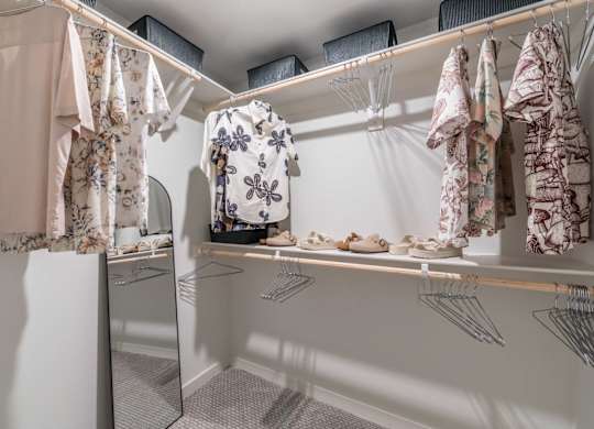 A white closet with clothes hanging and shoes on a shelf.