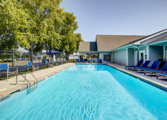 a swimming pool with blue chaise lounge chairs and a building in the background