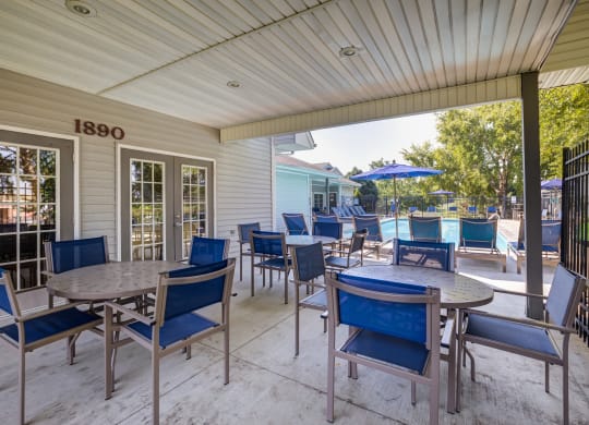 a covered patio with tables and chairs and a pool in the background