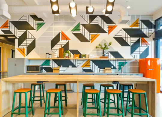 a long wooden table with green and orange stools in front of a white and black wall