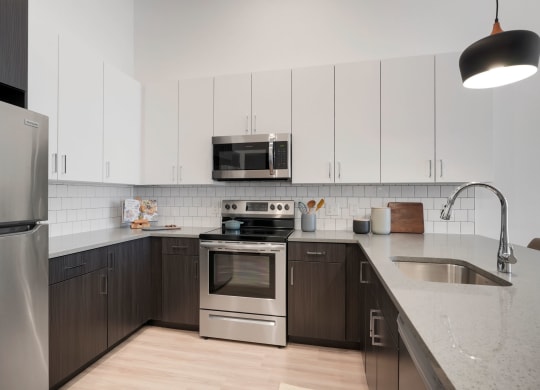 1 Bedroom Apartments In Wheat Ridge, CO - The Parallel - Gourmet Kitchen with White Upper Cabinets and Dark Brown Lower Cabinets, White Tile Backsplash, Quartz Countertops, Stainless Steel Appliances, and Luxury Plank Floors