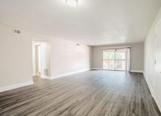 Living room with hardwood-style flooring, large window, and sliding door at Townsend Apartments in Jacksonville near Atlantic Beach, Florida.