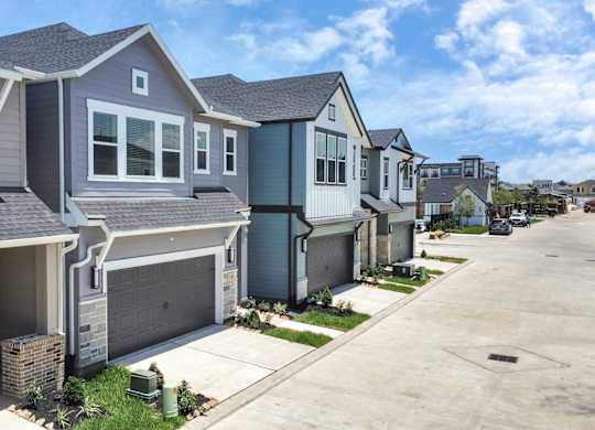 Houses for Rent in Heights, Houston, TX - The Crossings at Timbergrove - A Row of Houses with Attached Garages, a Driveway, and a Green Grass Area.
