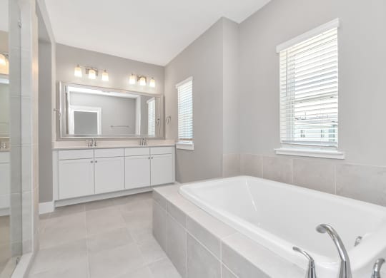 Heights, Houston, TX, Homes For Rent - The Crossing at Timbergrove - Bathroom with Bathtub, Tile Flooring, a Double Vanity with White Cabinets, and a Large Mirror.