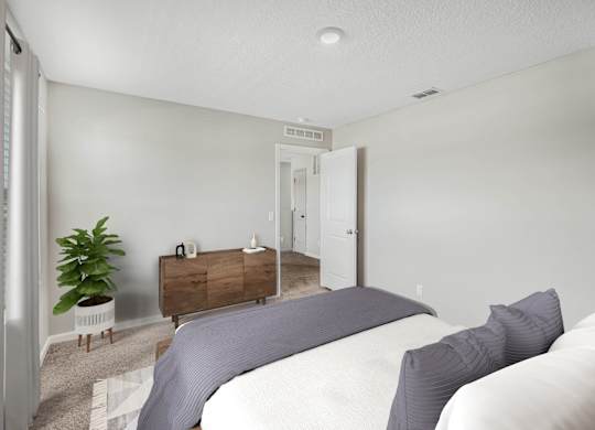 A bedroom with a bed, nightstand, and a plant.