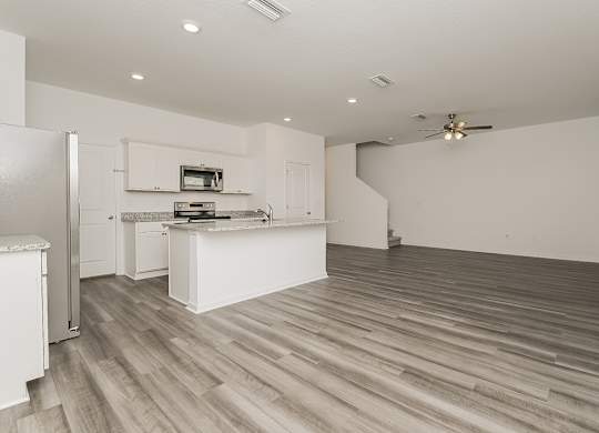 A kitchen with a refrigerator, stove, and wooden floors.