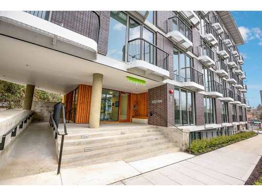 Fremont, WA Apartments For Rent - Inspire Fremont - Streetview Of The Building, Large Glass Windows, Wheelchair Ramp, Paved Side Walk, And White Balconies.