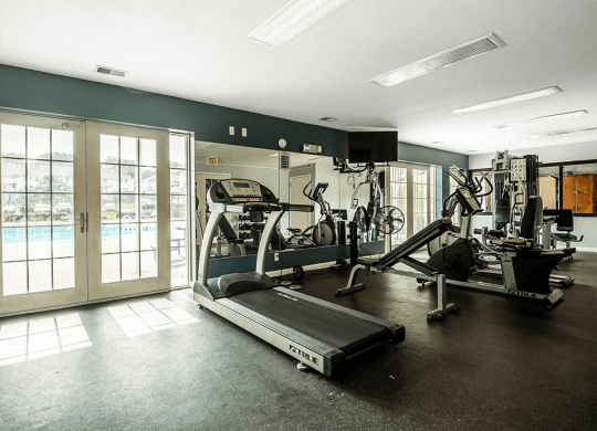 a gym with cardio equipment and a pool in the background