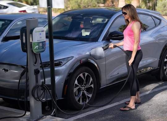 A woman is charging an electric car at a charging station.