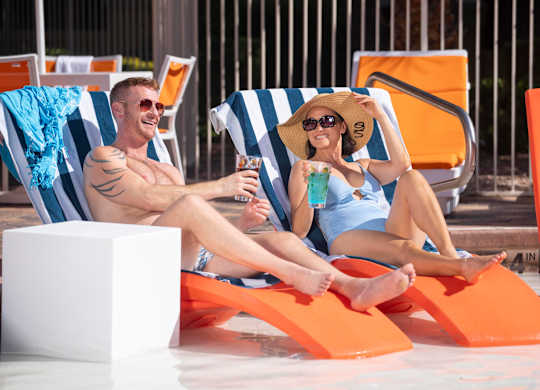 A man and a woman are sitting on beach chairs by the pool.