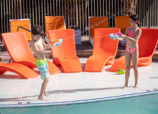 Two children playing with water guns by the pool.