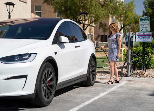 A woman is standing next to a white Tesla car at a charging station. at Habitat @ DTLV, Nevada, 89106