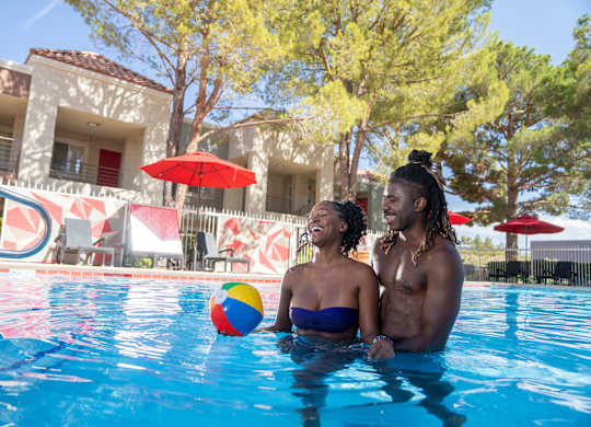 A couple is sitting in a pool with a ball in the foreground.
