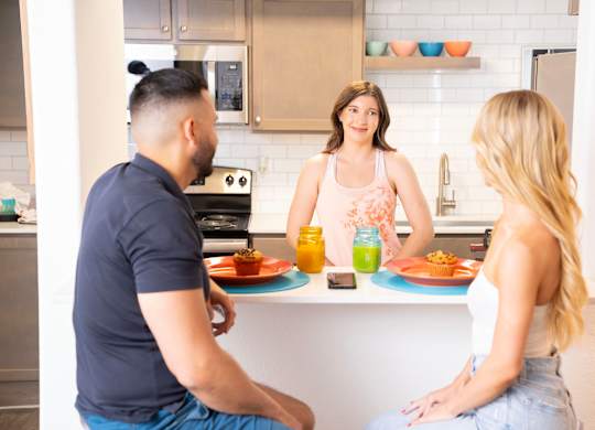 A man and two women are sitting at a kitchen island with food and drinks. at The 95 Apartments, Las Vegas, NV