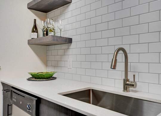 A kitchen with a white tiled wall and a stainless steel sink.