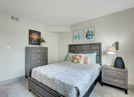 A bedroom with a bed, nightstand, and two pictures on the wall.