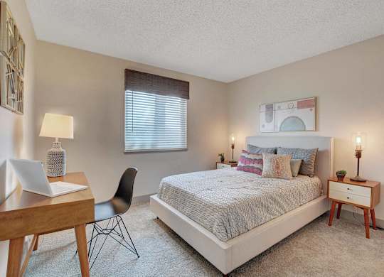 A bedroom with a bed, desk, chair, and window.