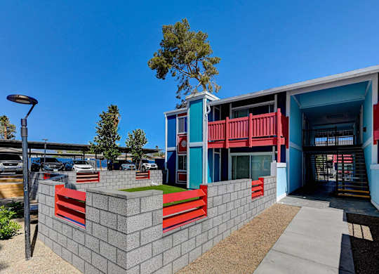 A modern building with a blue and red facade and a green tree in front.