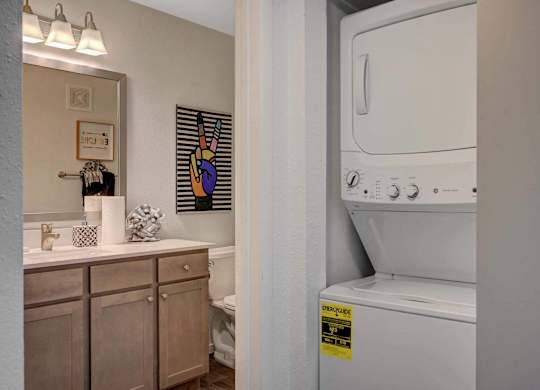A washing machine is in a small bathroom with a mirror, toilet, and sink.
