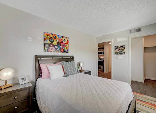 A bedroom with a bed, nightstand, and a painting on the wall.