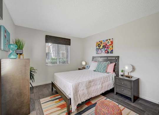 A bedroom with a bed, nightstand, and a plant.