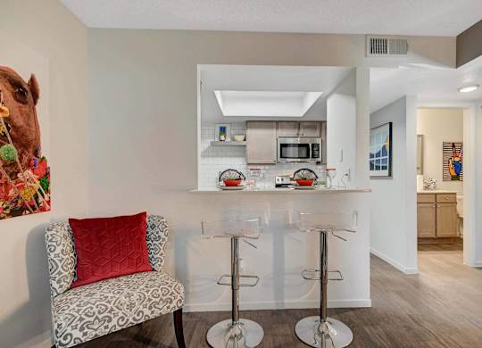 A kitchen with a bar stool and a chair with a red pillow.