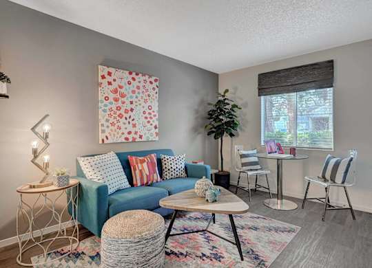 A living room with a blue couch, a white table, and a colorful rug.