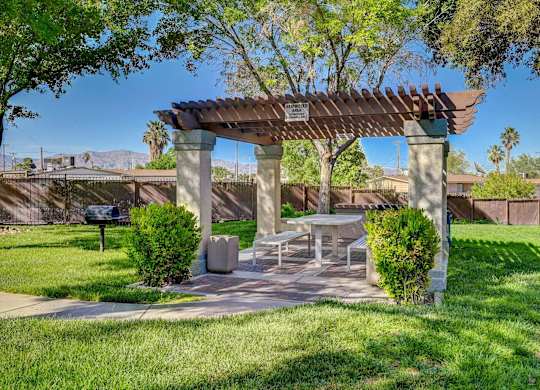 A park with a picnic table and a shaded area under a pergola.