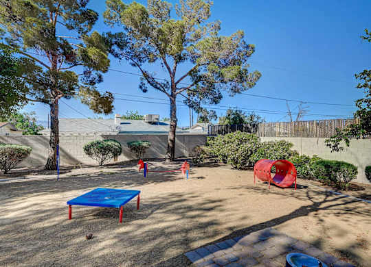 A backyard with a blue trampoline and a red tunnel.