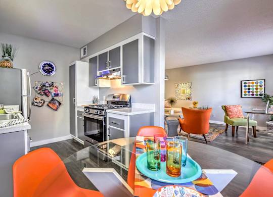 A modern kitchen with orange chairs and a dining table set for two.