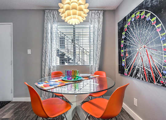 A dining room with a glass table and orange chairs.