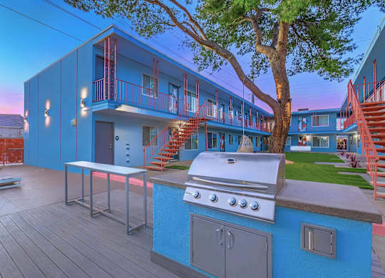 A blue house with a grill on the deck.