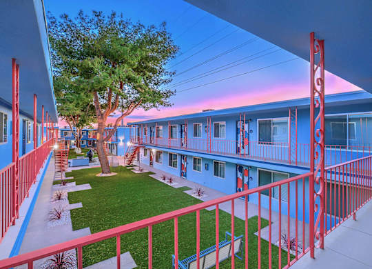 A tree is in front of a blue building with red railings.