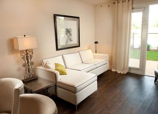 A white sofa with a yellow pillow is in the center of a room with a picture frame and a lamp on the side.