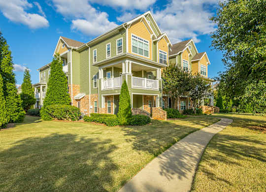 A large, multi-story residential building with a well-manicured lawn and a clear sky above.