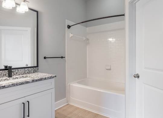 A white bathroom with a marble countertop and a white bathtub.